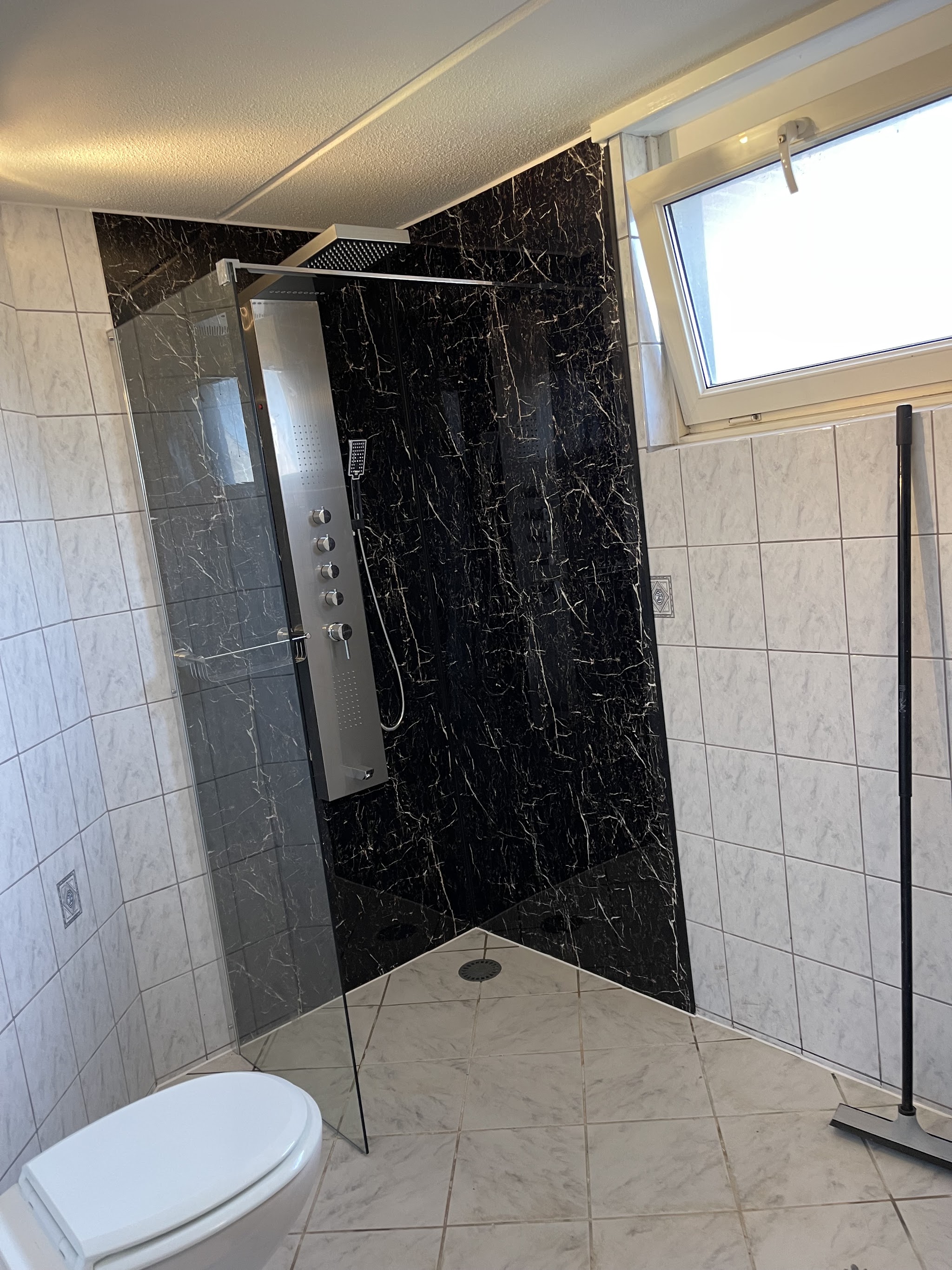 Afgewerkte badkamer met een zwart-marmeren douchewand en witte tegels